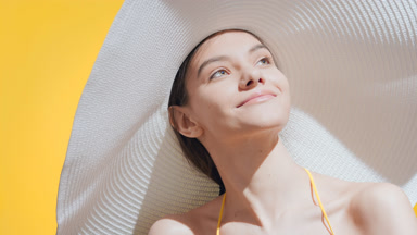 Young woman in a big white hat applies sunblock on her shoulder