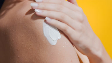 Woman in a yellow swimwear applies sun cream on her shoulder