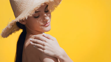 Woman in a yellow swimsuit applies spf cream on her shoulder