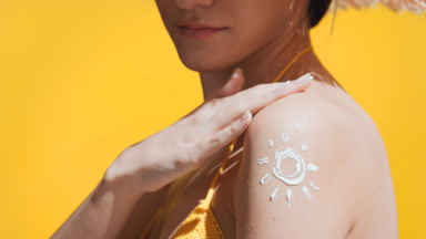 Woman in a yellow crochet swimwear puts sunscreen on shoulder