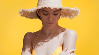 Woman in a crochet beachwear puts sunscreen on shoulder smiling