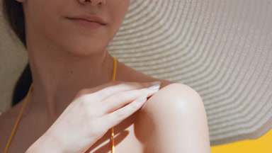 Young woman in a big white hat puts sunblock on her shoulder