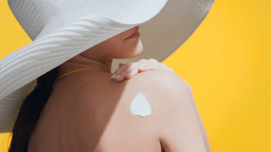 Woman applies sunblock on her shoulder, turns and enjoys the sun