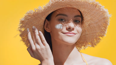 Young woman puts sun cream on cheek, enjoys the sun and smiles