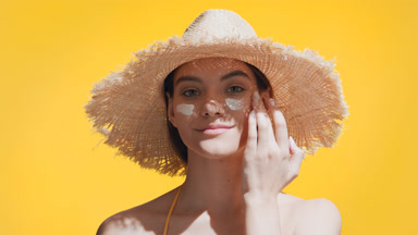 Young woman puts spf cream on cheeks, enjoys the sun and smiles