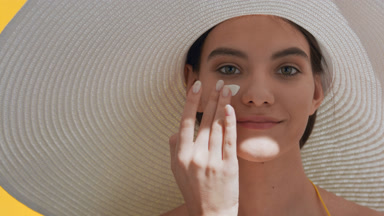 Brunette woman in a big white hat applies sun cream on cheek