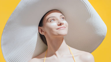 Woman in a big white hat applies sunblock on cheeks smiling wide