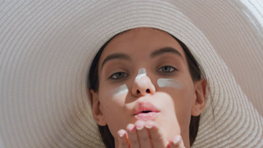 Woman with sunscreen on her cheeks and nose blows a kiss