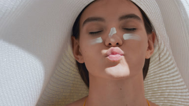 Young woman with sun cream on her cheeks and nose blows a kiss