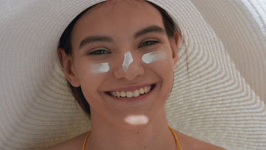 Happy young woman with spf cream on her cheeks and nose laughing