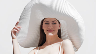 Woman in a white hat enjoys the sun holding her hat and smiling