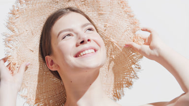 Caucasian woman puts a straw hat on enjoying the sun and smiling