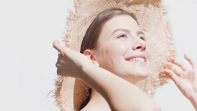 Young woman puts a straw hat on turning to the sun to enjoy it