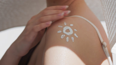 Young fit woman in a white hat applies sunscreen on her shoulder