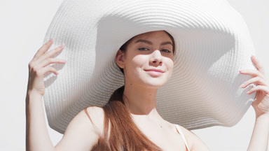 Woman in a hat applies sunblock on shoulder and enjoys the sun
