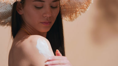 Girl applying sunscreen on her shoulder and looks at the camera