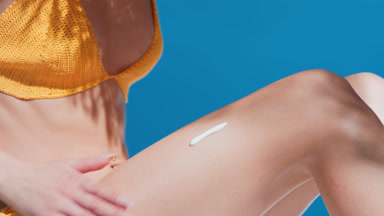 Young woman in yellow bikini putting sunblock on her leg