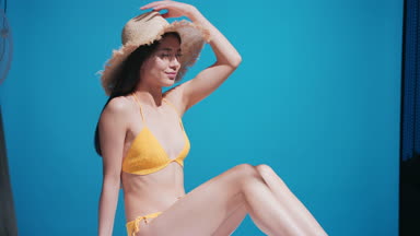 Young woman in yellow swimwear putting a straw hat on her head