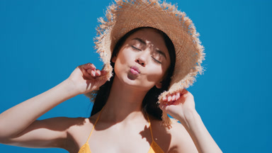 Young female model in straw hat enjoys the sun and blows a kiss