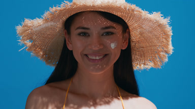 Young Asian woman puts some sunscreen on her cheek and smiles