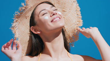 Young woman in a straw hat puts some sunscreen on her cheeks
