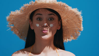 Young woman in a straw hat puts some sunscreen on her nose