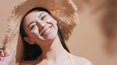 Young woman in straw hat applies some sunscreen on her nose