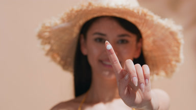 Woman shows a drop of sunscreen cream and applies it to her face