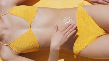 Fit woman in bikini lying on blanket applies sunscreen on belly