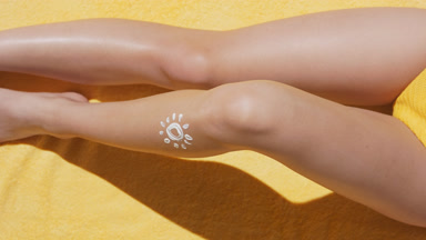 Woman in swimsuit sitting on blanket puts sunblock on her leg