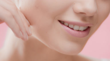 Female skincare model touches her jawline smiling for the camera