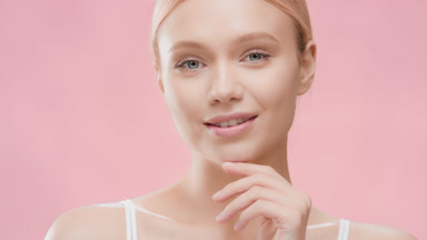 Blonde woman with ponytail turns to the camera touching her face