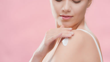 Woman applies moisturizer on shoulder and smiles for the camera