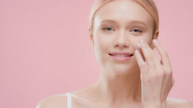 Attractive woman applies moisturizer on cheek smiling for camera