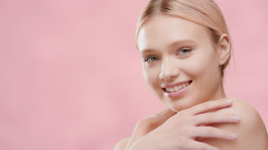 Blonde skin care woman touches her body smiling wide for camera