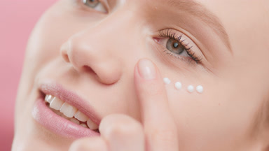 Female skincare model applies eye cream smiling wide for camera