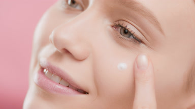 Female skin care model puts eye cream on face smiling for camera