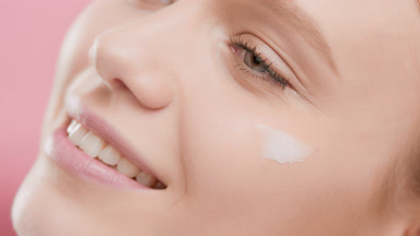 Beauty woman applies moisturizer on face smiling wide for camera