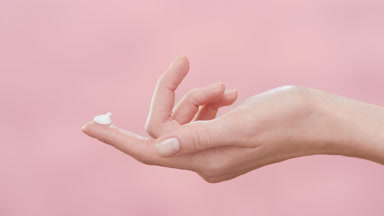 Female model lifts hand with a blob of cream on forefinger up