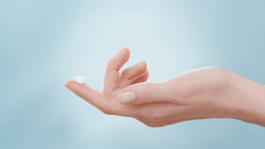 Model lifts hand with a drop of cream on forefinger up and down