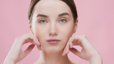 Woman opens eyes touching jawline and smiles looking at camera