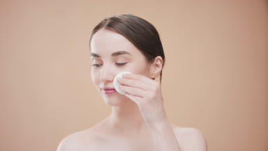 Caucasian girl touches cheek with cotton pad looking at camera