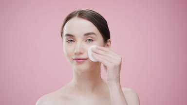 European woman touches cheek with cotton pad looking at camera