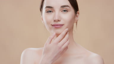 Gorgeous woman with bare shoulders touches jawline turning body
