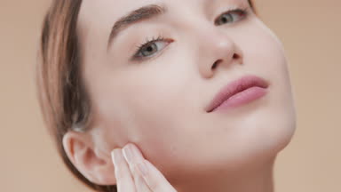 Beautiful woman touches face and smiles wide looking at camera