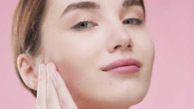 Attractive woman touches face and smiles wide looking at camera