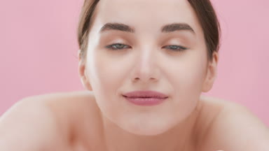 Dark-haired woman lies head on arm looking at camera and smiling