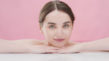 Female skin care model with bare shoulders puts head on hands