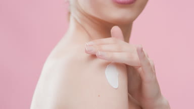 Good-looking female model applies moisturizer on her shoulder