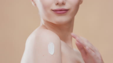Cute girl with bare shoulders puts moisturizer on her shoulder